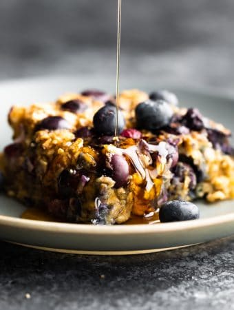 close up shot of a slice of blueberry baked oatmeal with syrup drizzled on top