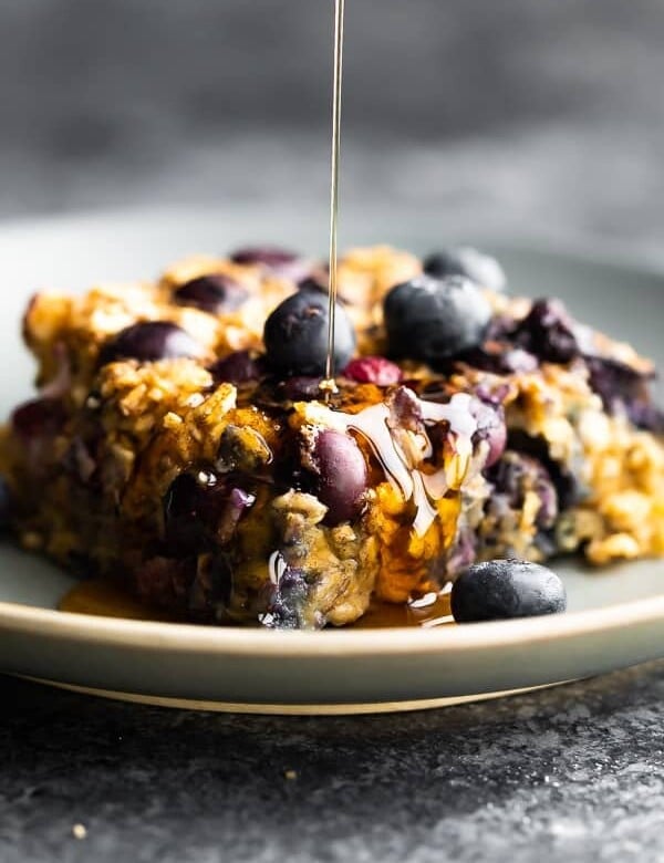 close up shot of a slice of blueberry baked oatmeal with syrup drizzled on top