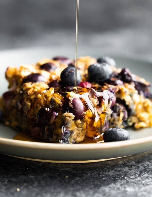 close up shot of a slice of blueberry baked oatmeal with syrup drizzled on top