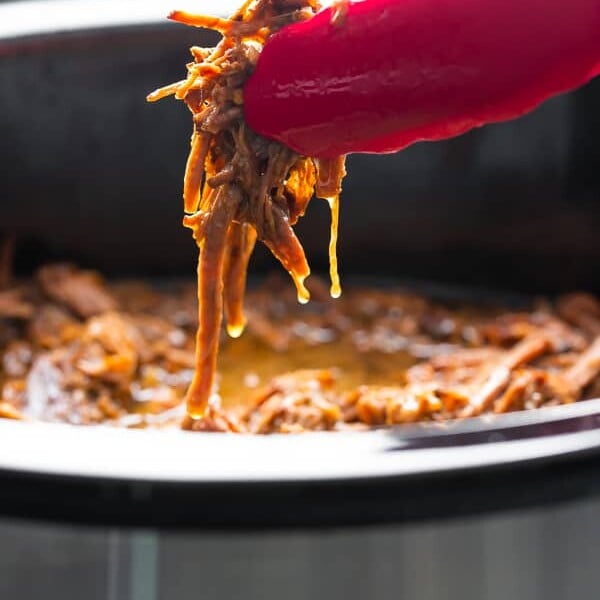 tongs pulling honey garlic beef out of the slow cooker
