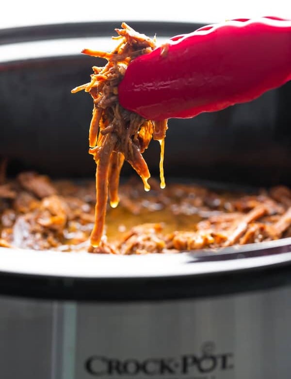tongs pulling honey garlic beef out of the slow cooker