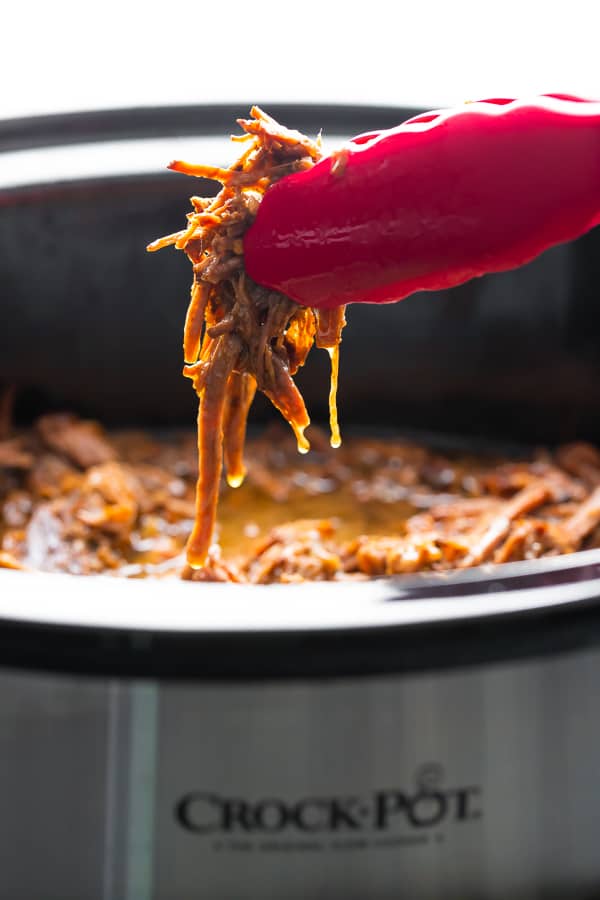 tongs pulling honey garlic beef out of the slow cooker