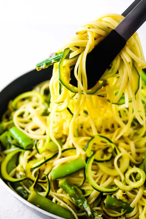tongs pulling pasta and spiralized zucchini out of skillet