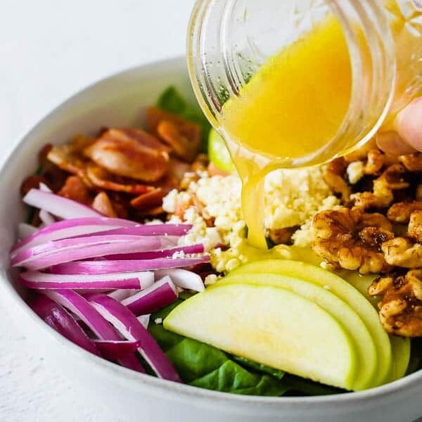 pouring vinaigrette over apple bacon spinach salad