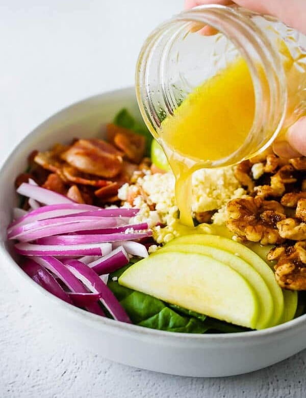 pouring vinaigrette over apple bacon spinach salad