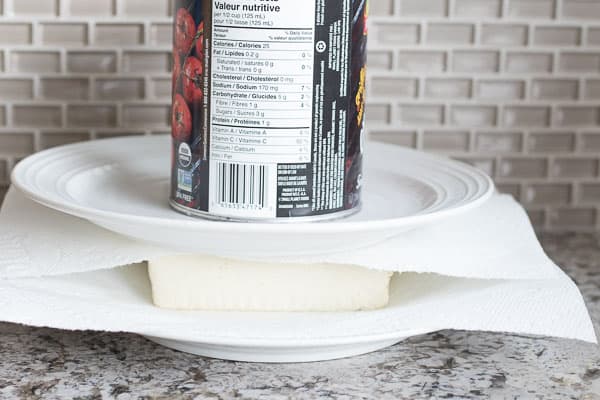 tofu pressed between plates with can on top