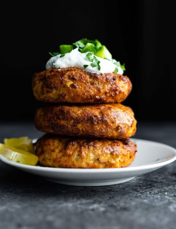 stack of air fryer salmon patties topped with yogurt and cucumbers