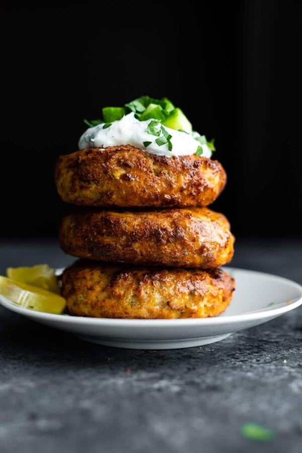 stack of air fryer salmon patties topped with yogurt and cucumbers