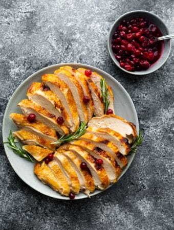 sliced turkey breast on plate with rosemary and cranberry sauce