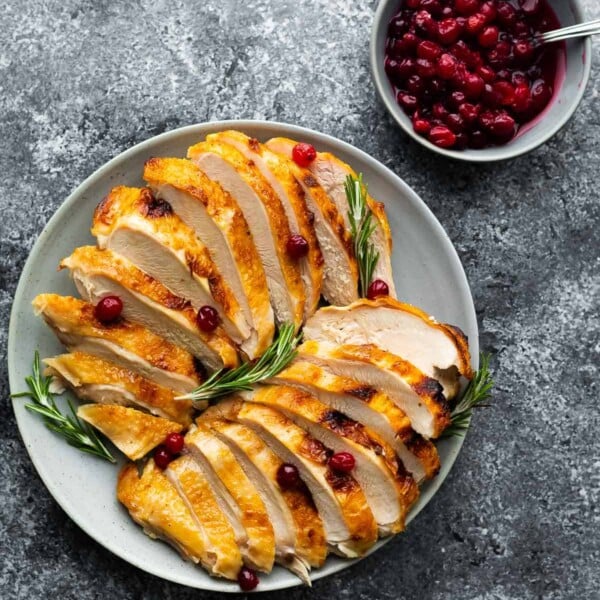 sliced turkey breast on plate with rosemary and cranberry sauce