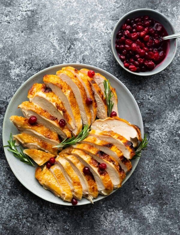 sliced turkey breast on plate with rosemary and cranberry sauce