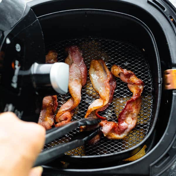 tongs flipping bacon in the air fryer