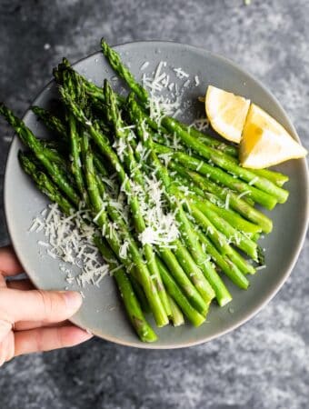 holding plate of asparagus with parmesan cheese