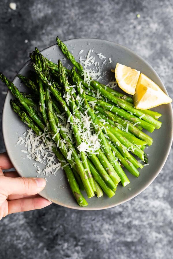 holding plate of asparagus with parmesan cheese