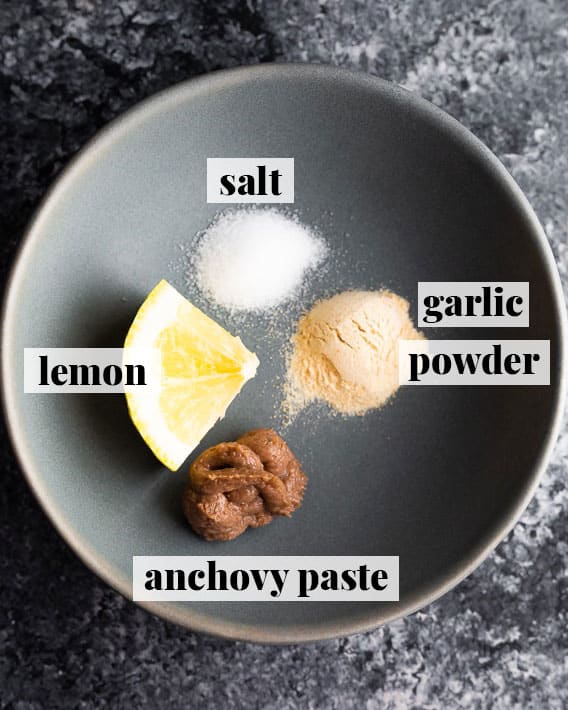 lemon, salt, anchovy paste, and garlic powder on a grey plate, from overhead
