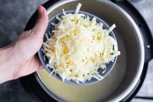 holding a bowl of shredded cheese over instant pot