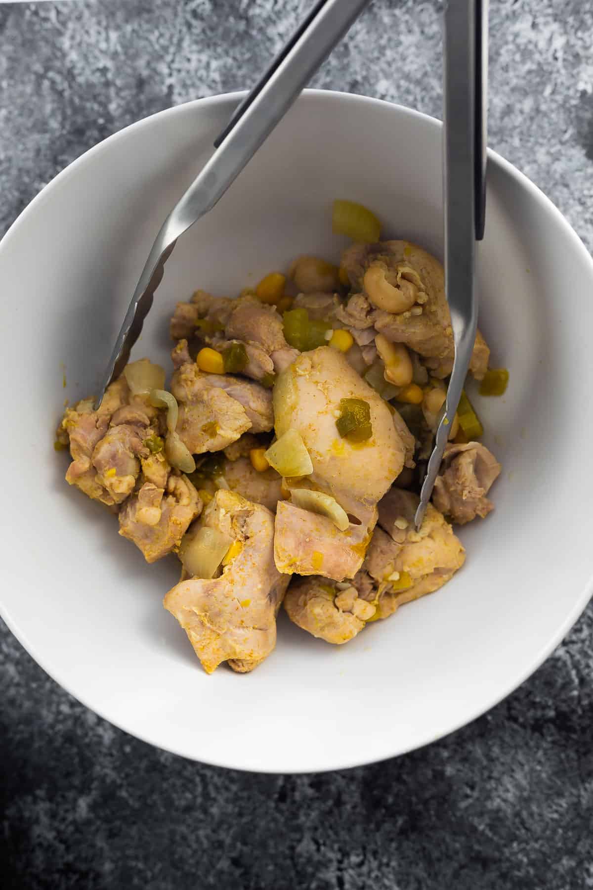 chicken thighs in white bowl with tongs