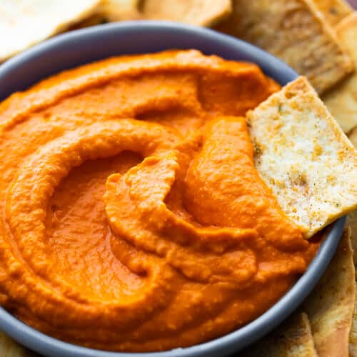 close up shot of roasted red pepper hummus with pita chip