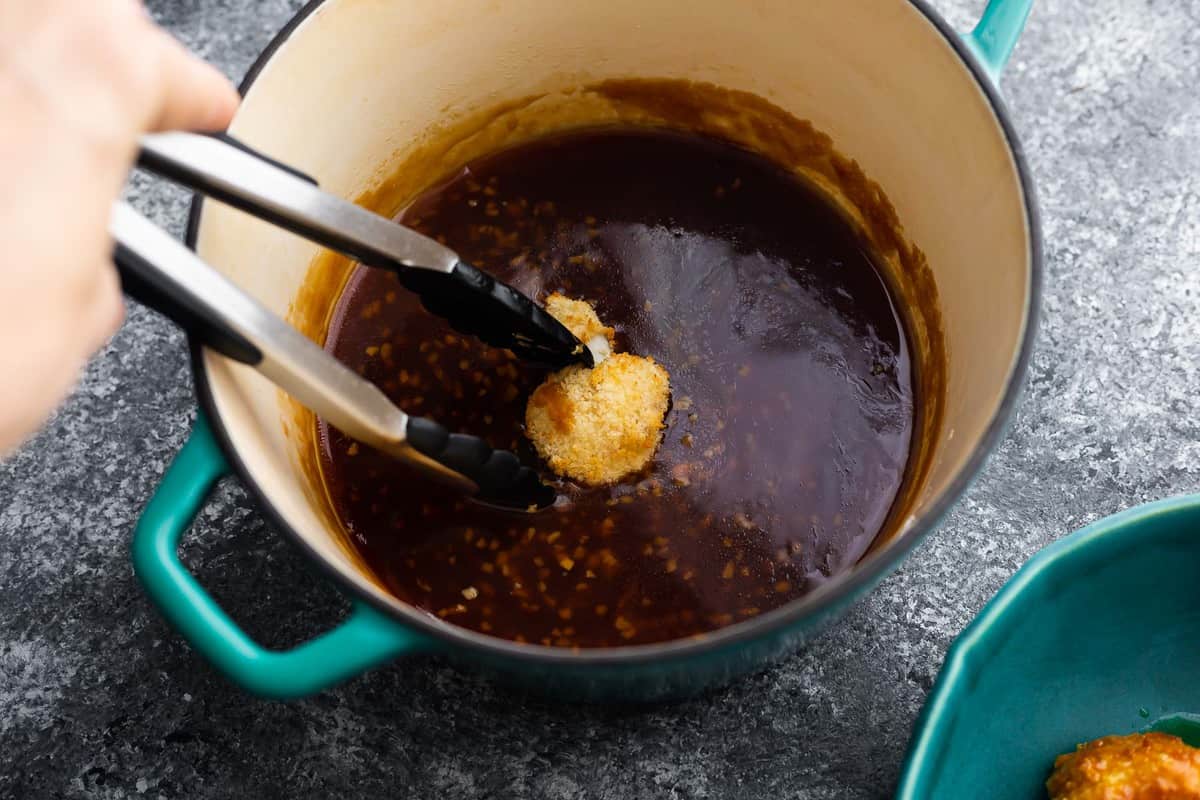 dipping breaded cauliflower into the honey garlic sauce with tongs