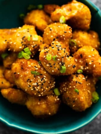 close up shot of air fryer cauliflower wings in blue bowl with sesame seeds and green onions as a garnish