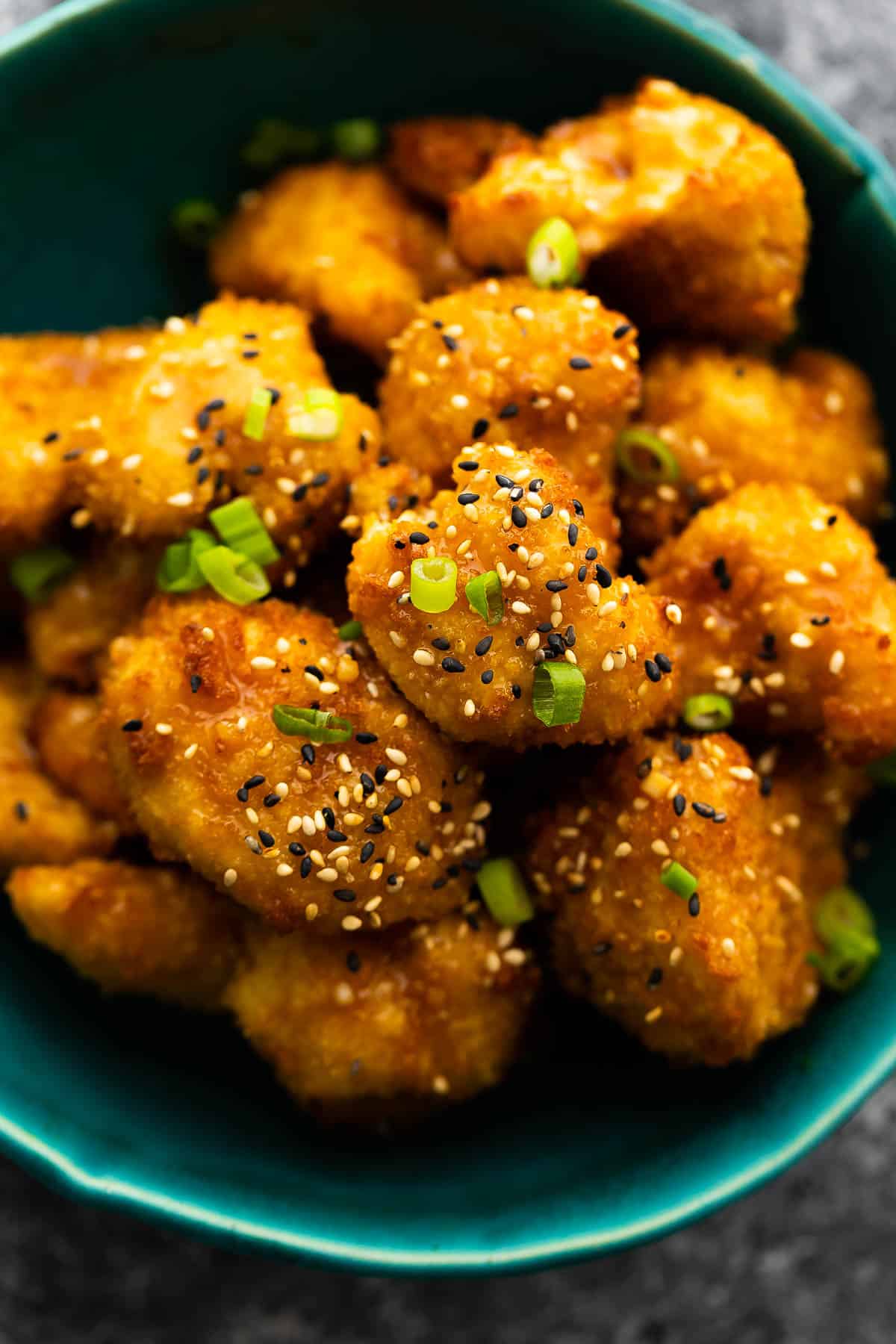 close up shot of air fryer cauliflower wings in blue bowl with sesame seeds and green onions as a garnish
