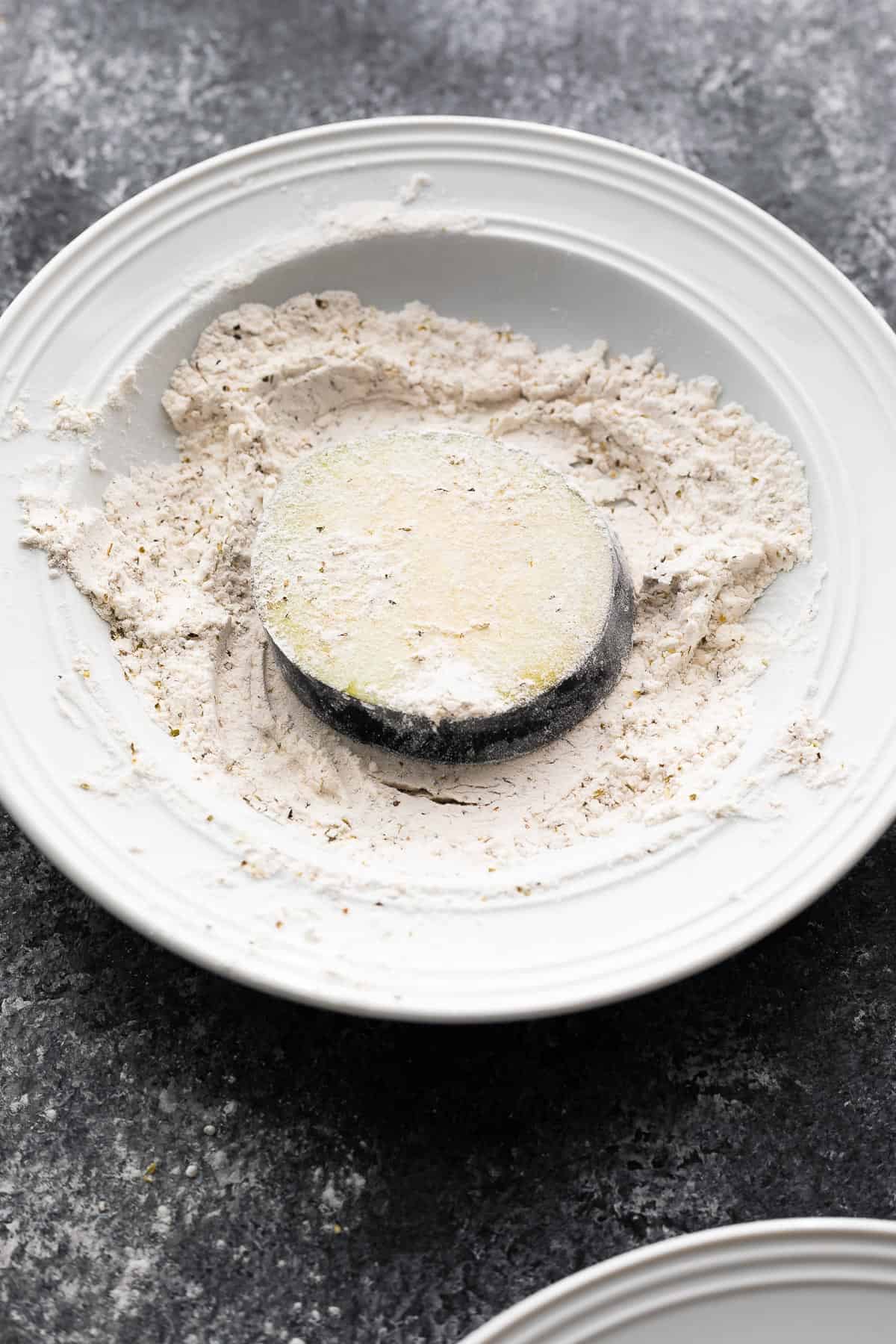 eggplant slice coated in flour mixture in a white bowl