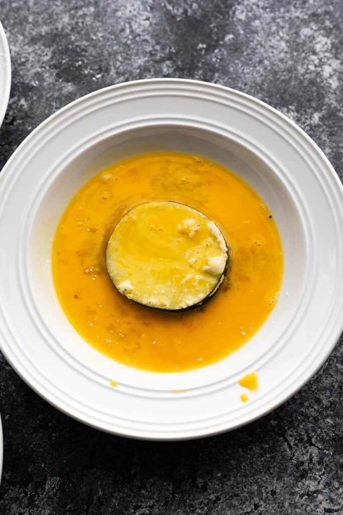 eggplant slice coated in egg in a white bowl