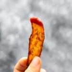 hand holding potato wedge dipped in ketchup