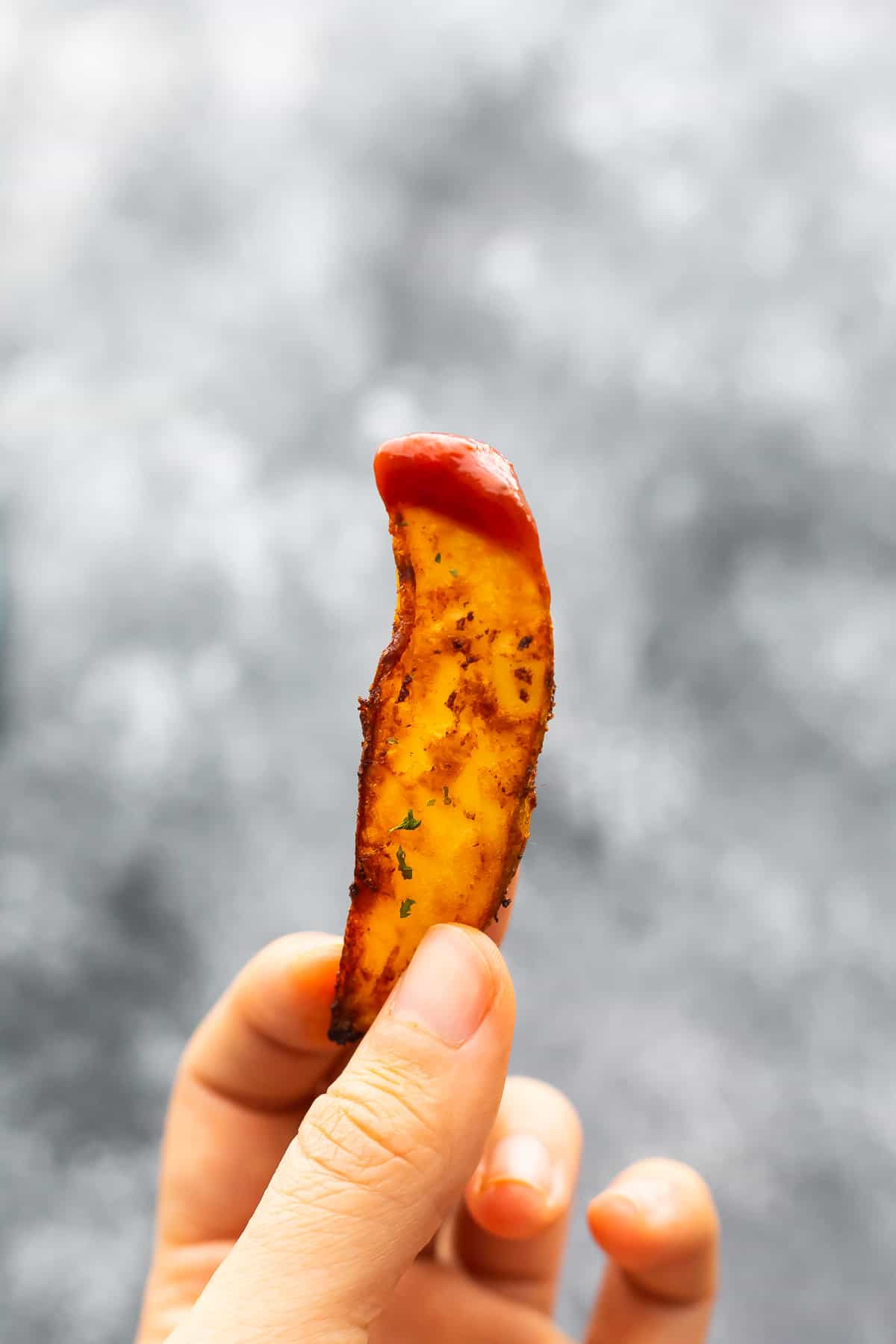 hand holding potato wedge dipped in ketchup