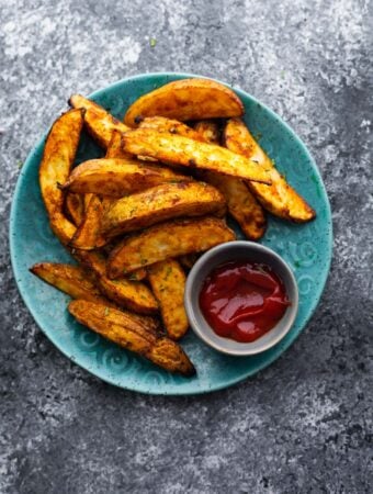cooked potato wedges arranged on blue plate with small bowl of ketchup