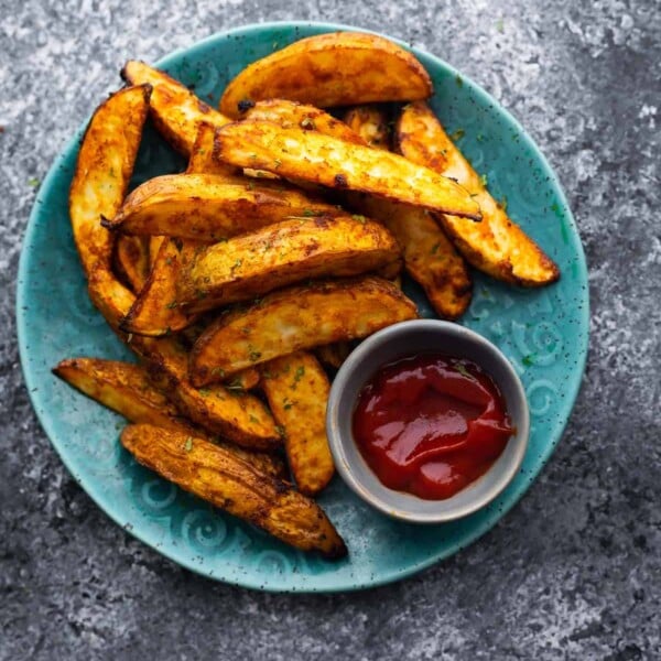 cooked potato wedges arranged on blue plate with small bowl of ketchup