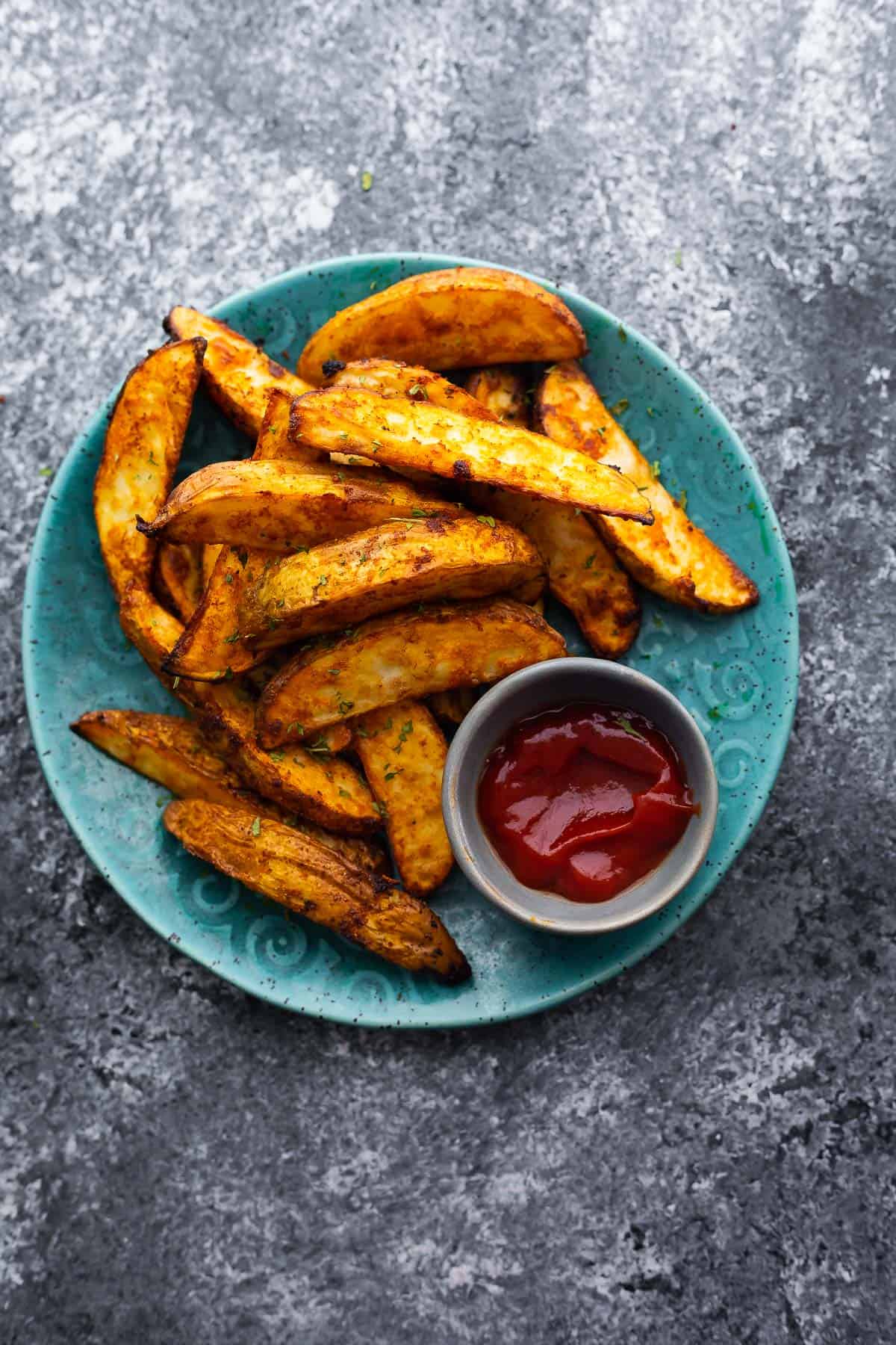 cooked potato wedges arranged on blue plate with small bowl of ketchup
