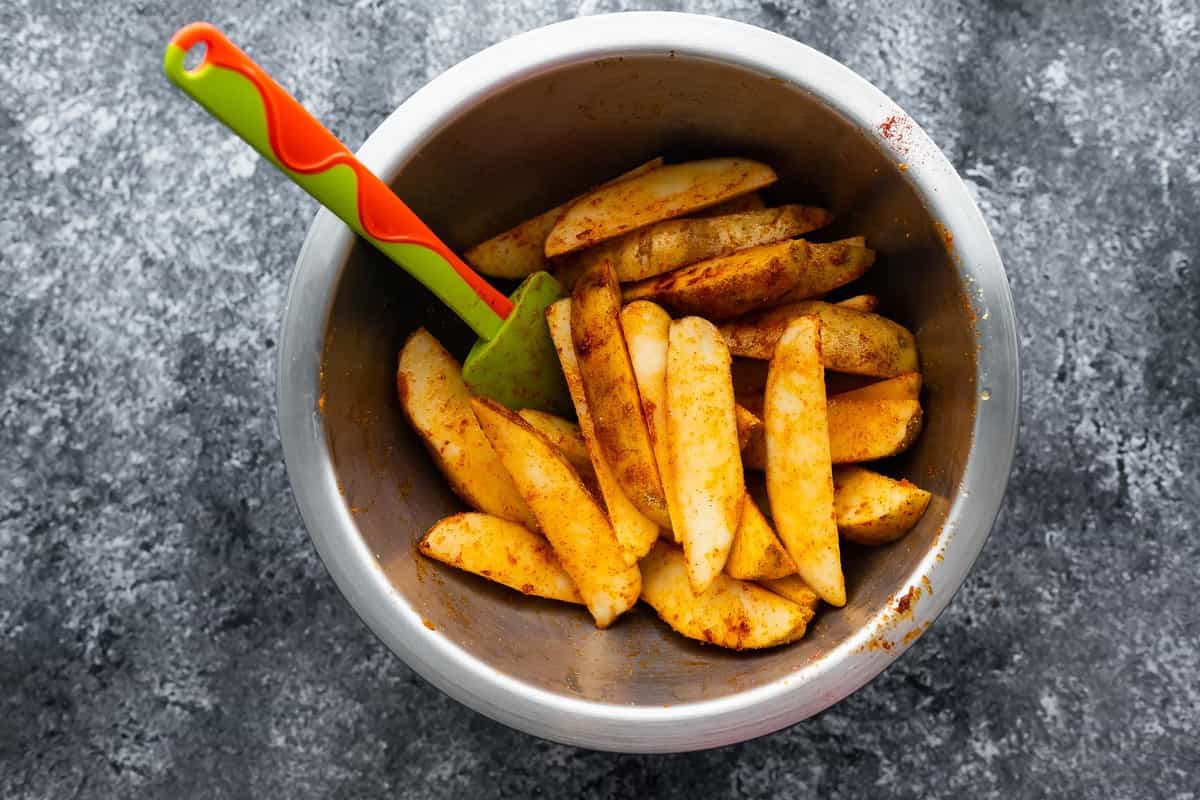 uncooked potato wedges in bowl tossed in spices