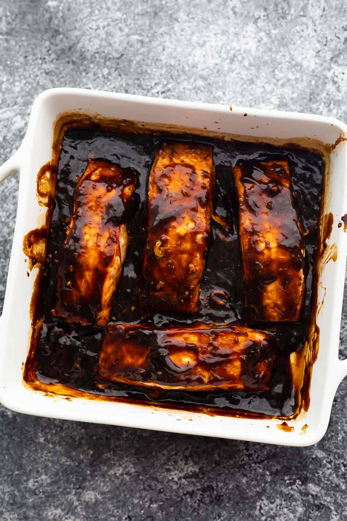 four baked salmon fillets arranged in baking dish with thickened teriyaki sauce