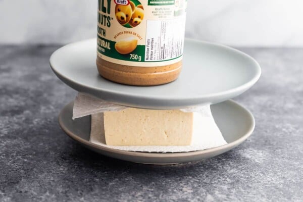 tofu pressed between paper towels, plates and with a jar of peanut butter on top