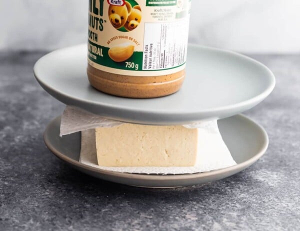 tofu pressed between paper towels, plates and with a jar of peanut butter on top