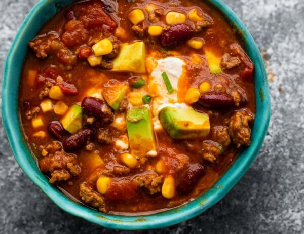 instant pot chili in blue bowl garnished with sour cream, cheese and avocado