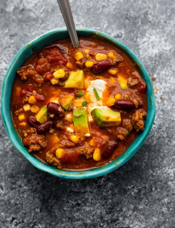 instant pot chili in blue bowl garnished with sour cream, cheese and avocado