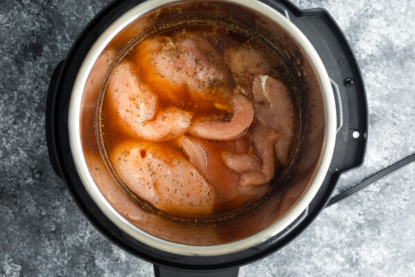 uncooked chicken breast in the instant pot with liquids and spices