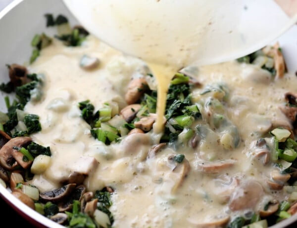 pouring eggs over sauteed mushrooms, kale and onion