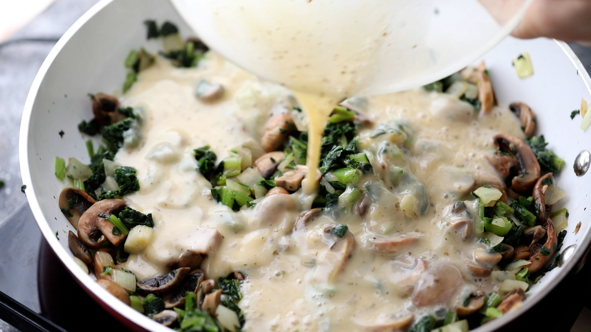 pouring eggs over sauteed mushrooms, kale and onion