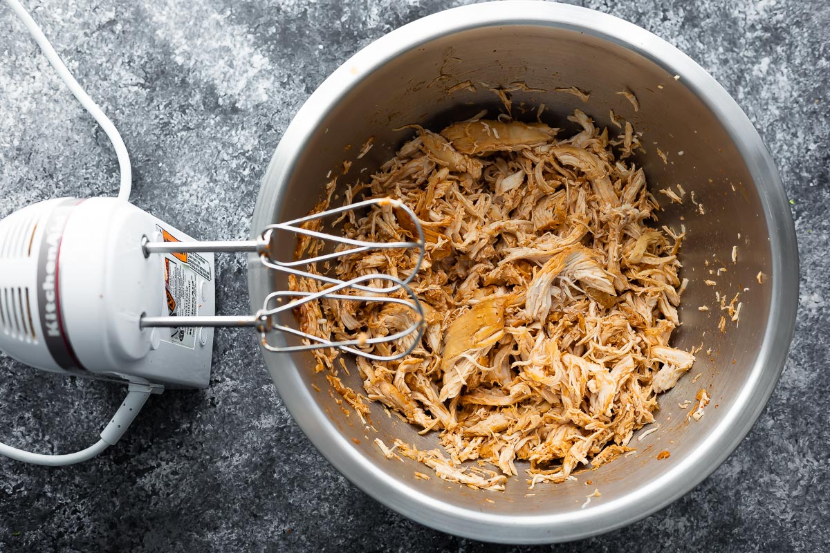 shredded chicken in a bowl with electric hand mixer sitting beside it