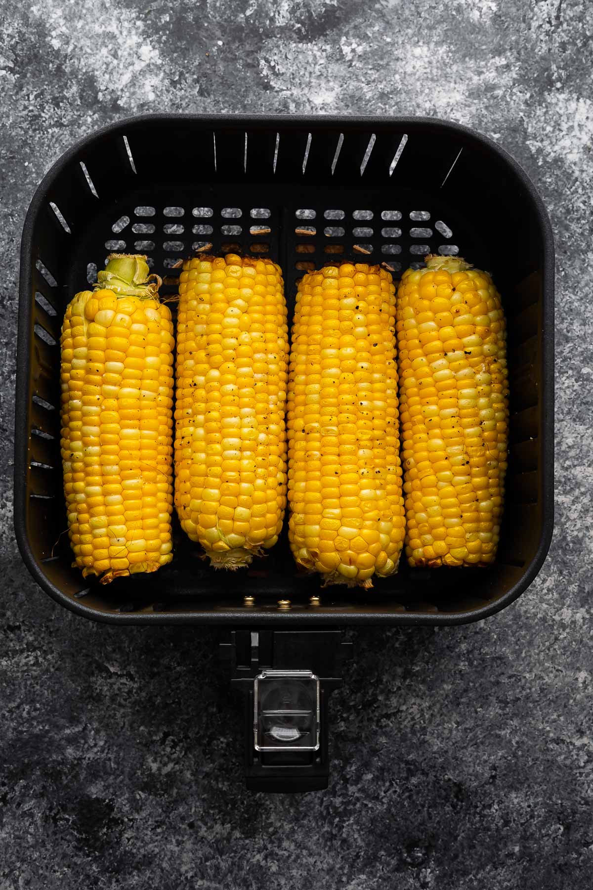 overhead view of four ears of corn in the air fryer basket (after cooking)