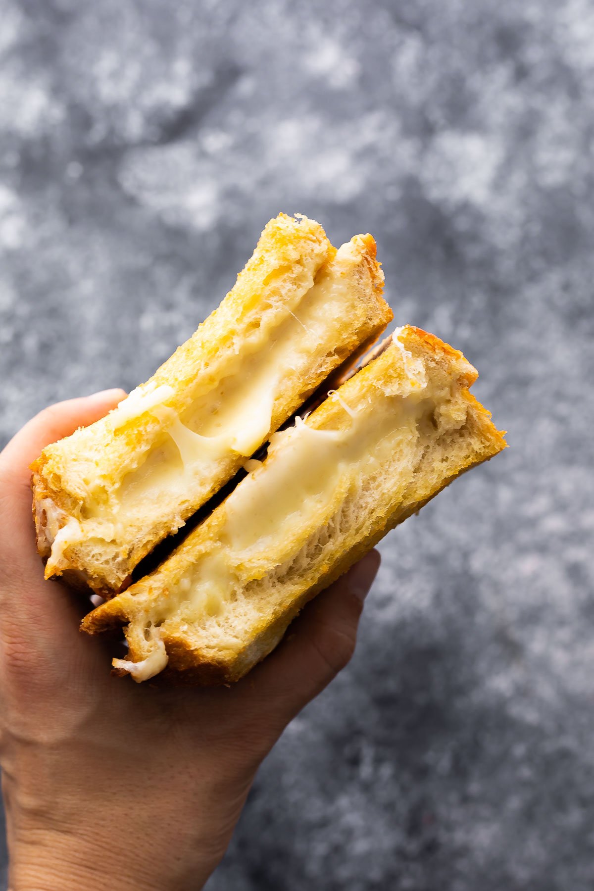 hand holding two pieces of grilled cheese revealing gooey cheese