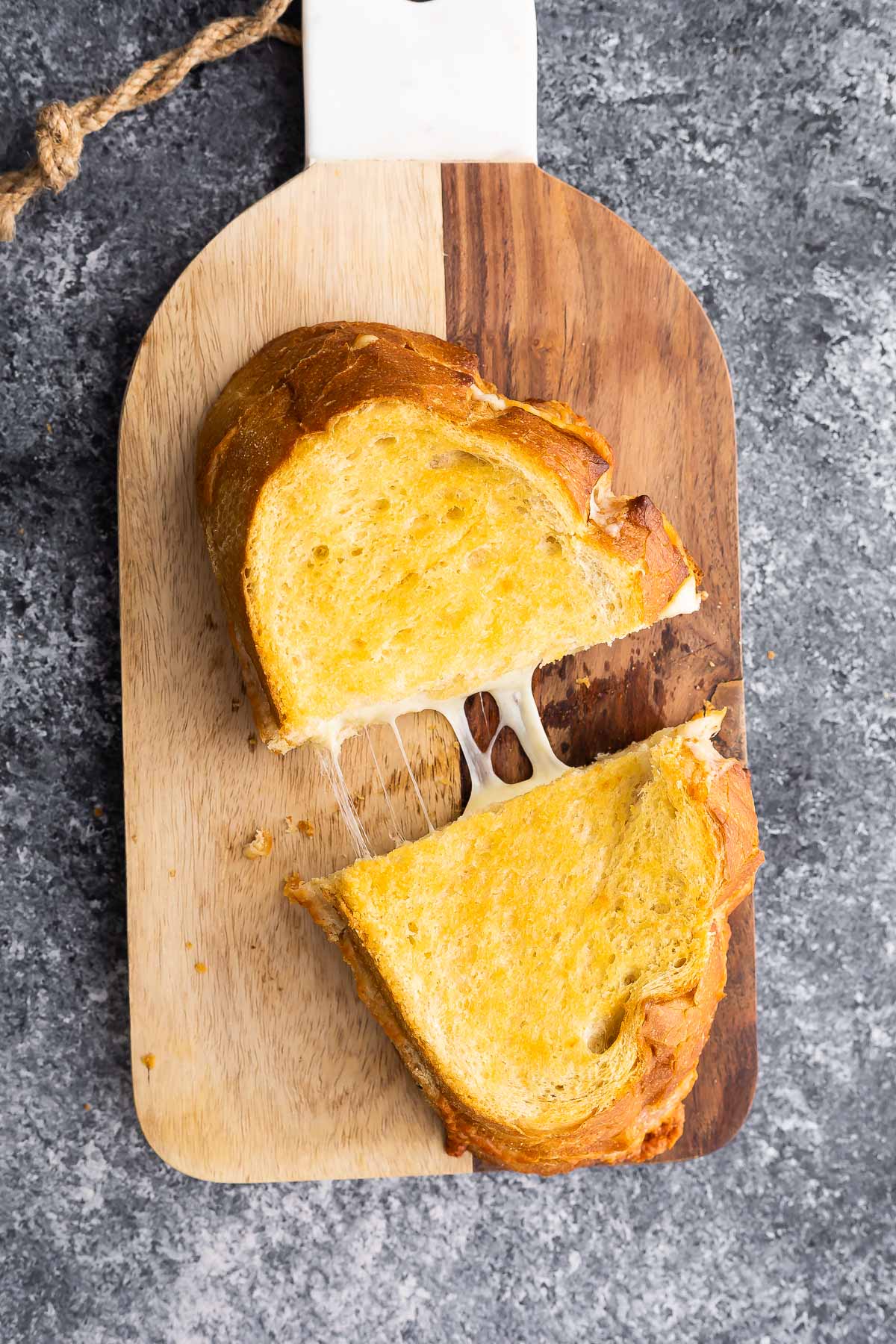 grilled cheese on cutting board, pulled apart revealing gooey cheese