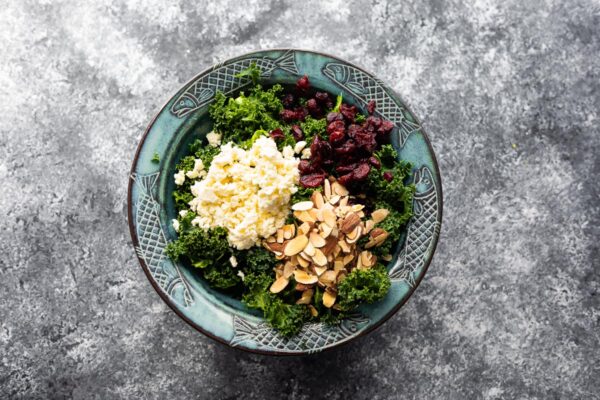 kale in salad bowl with almonds, cranberries and feta cheese