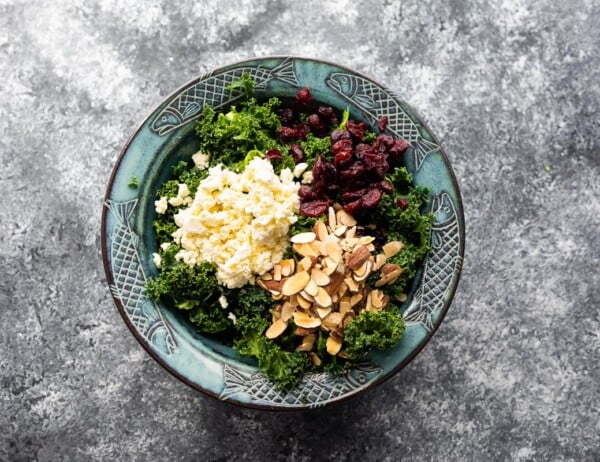 kale in salad bowl with almonds, cranberries and feta cheese