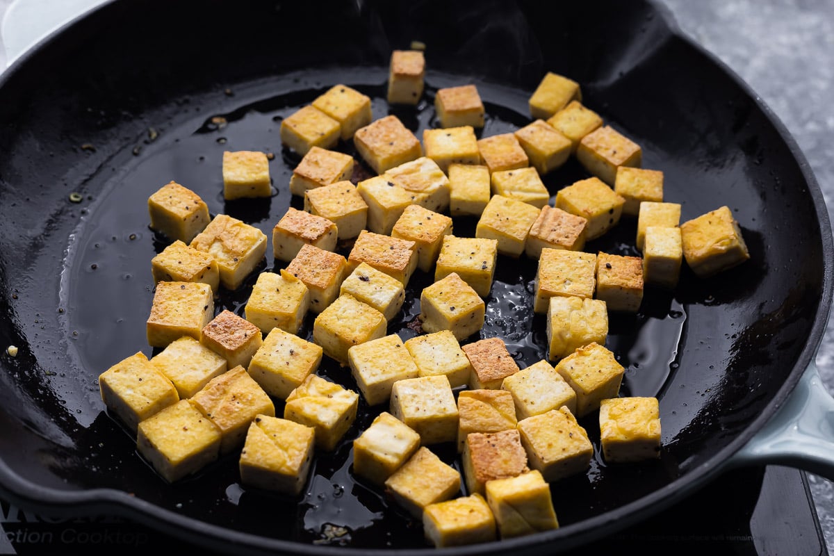 golden, crispy tofu being fried in pan with oil