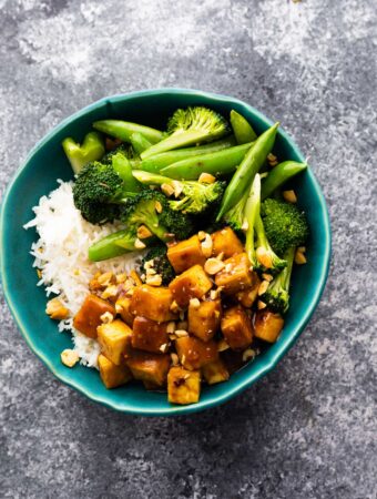 overhead view of peanut tofu in bowl with rice and green vegetables