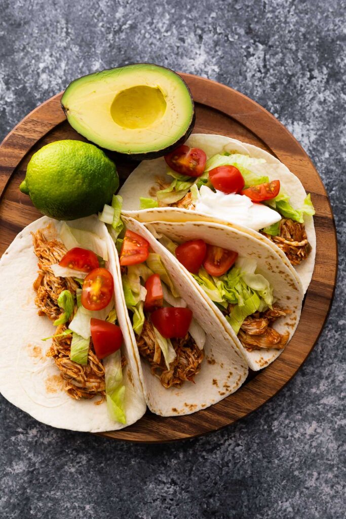 tacos made with salsa chicken, lettuce, tomatoes and sour cream on wooden board